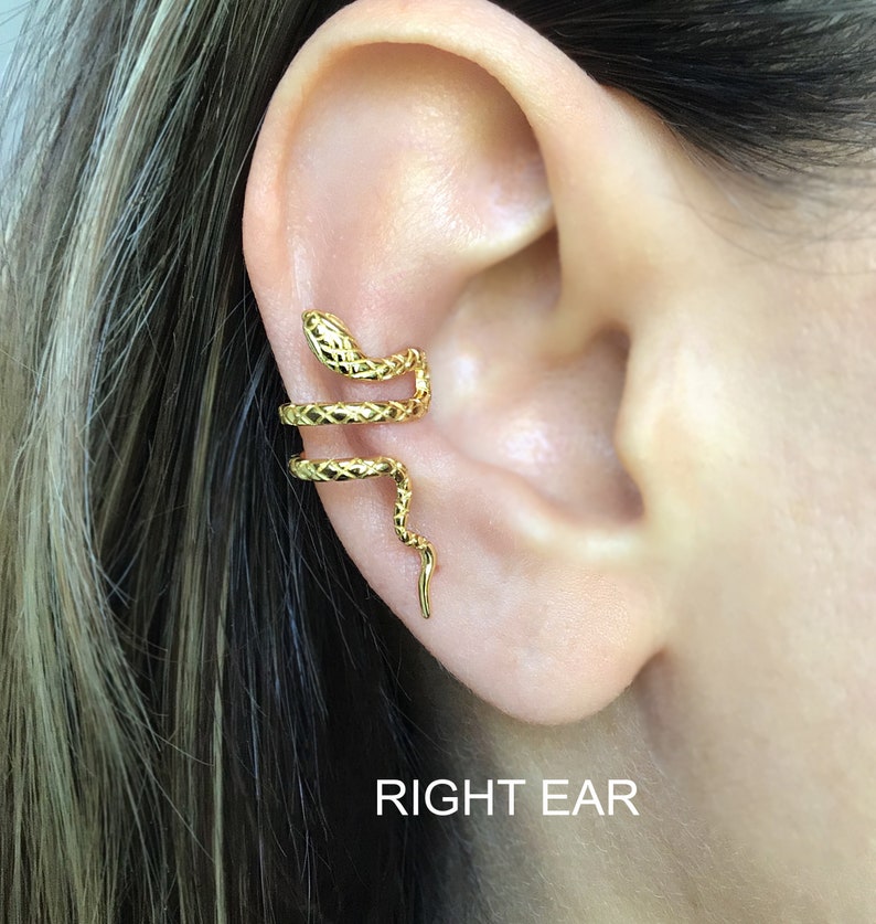 Puede incluir: Un pendiente de oreja de serpiente dorado. La serpiente est&aacute; enroscada alrededor de la oreja y tiene una superficie texturizada. El pendiente de oreja est&aacute; dise&ntilde;ado para ser usado en la oreja derecha. El texto "RIGHT EAR" es visible debajo del pendiente de oreja.