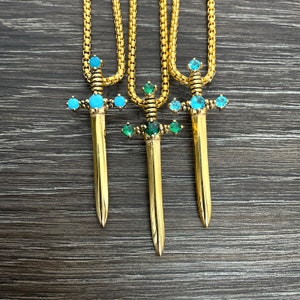 May include: Three gold sword pendants with blue and green gemstones hanging from gold chains.