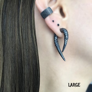 Peut inclure: Une boucle d'oreille noire en forme de griffe avec une surface textur&eacute;e. La boucle d'oreille est port&eacute;e dans le lobe sup&eacute;rieur de l'oreille. La boucle d'oreille est &eacute;tiquet&eacute;e "LARGE".