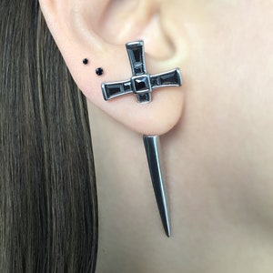 May include: A pair of silver earrings with a black cross design and a long, pointed silver dagger pendant.