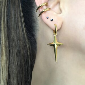 May include: Gold star-shaped earring with a hoop and two small black gemstone studs in the earlobe.