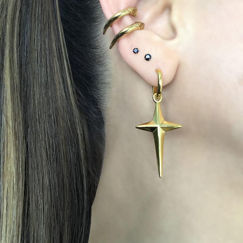May include: Gold star-shaped earring with a hoop and two small black gemstone studs in the earlobe.