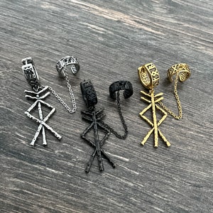 May include: Four ear cuff earrings in silver, black, and gold tones. Each earring features a geometric pendant and a cuff connected by a chain. The cuffs have intricate patterns.