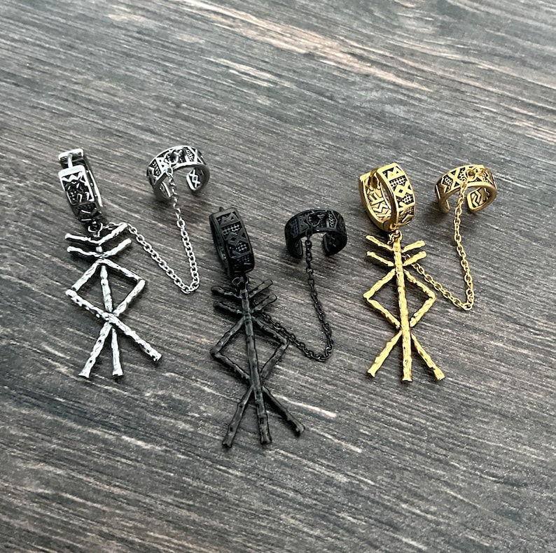 May include: Four ear cuff earrings in silver, black, and gold tones. Each earring features a geometric pendant and a cuff connected by a chain. The cuffs have intricate patterns.