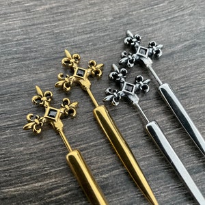 Pu&ograve; includere: Tre orecchini in oro e argento con una pietra nera al centro di un design a giglio.