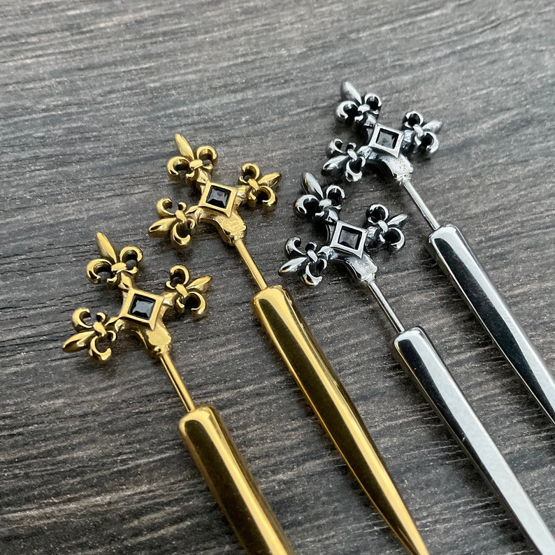 Pu&ograve; includere: Tre orecchini in oro e argento con una pietra nera al centro di un design a giglio.