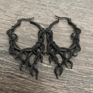 May include: A pair of black hoop earrings with an octopus tentacle design. The earrings are made of metal and have a shiny finish.