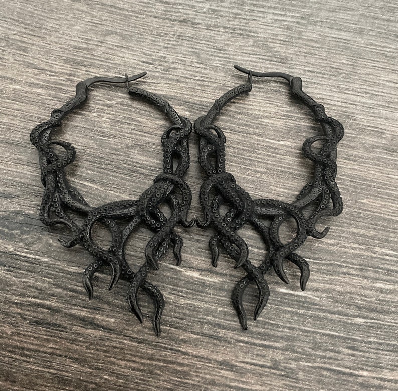 May include: A pair of black hoop earrings with an octopus tentacle design. The earrings are made of metal and have a shiny finish.