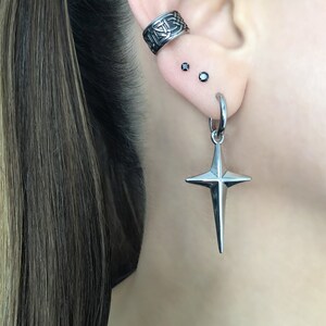 May include: A silver star-shaped earring with a hoop and a small black gemstone on the earlobe.