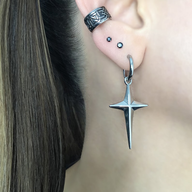May include: A silver star-shaped earring with a hoop and a small black gemstone on the earlobe.