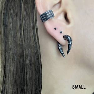 Peut inclure: Boucles d'oreilles en forme de griffe noires avec un anneau noir sur l'oreille sup&eacute;rieure. Les boucles d'oreilles sont en m&eacute;tal et ont une finition textur&eacute;e.