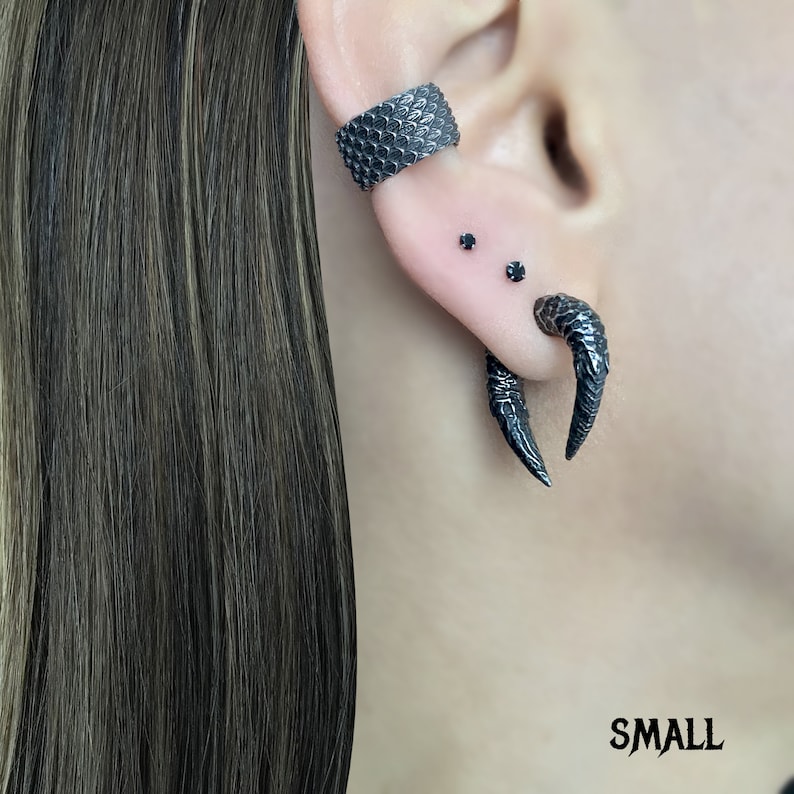 Peut inclure: Boucles d'oreilles en forme de griffe noires avec un anneau noir sur l'oreille sup&eacute;rieure. Les boucles d'oreilles sont en m&eacute;tal et ont une finition textur&eacute;e.
