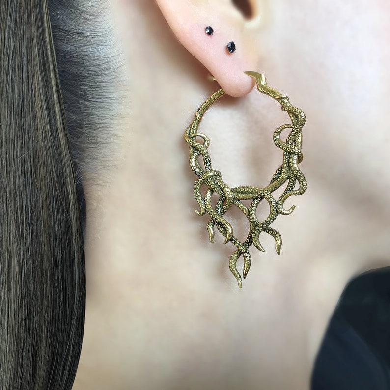 May include: Gold-toned hoop earrings with a dangling design resembling a cluster of snake or tentacle-like shapes.