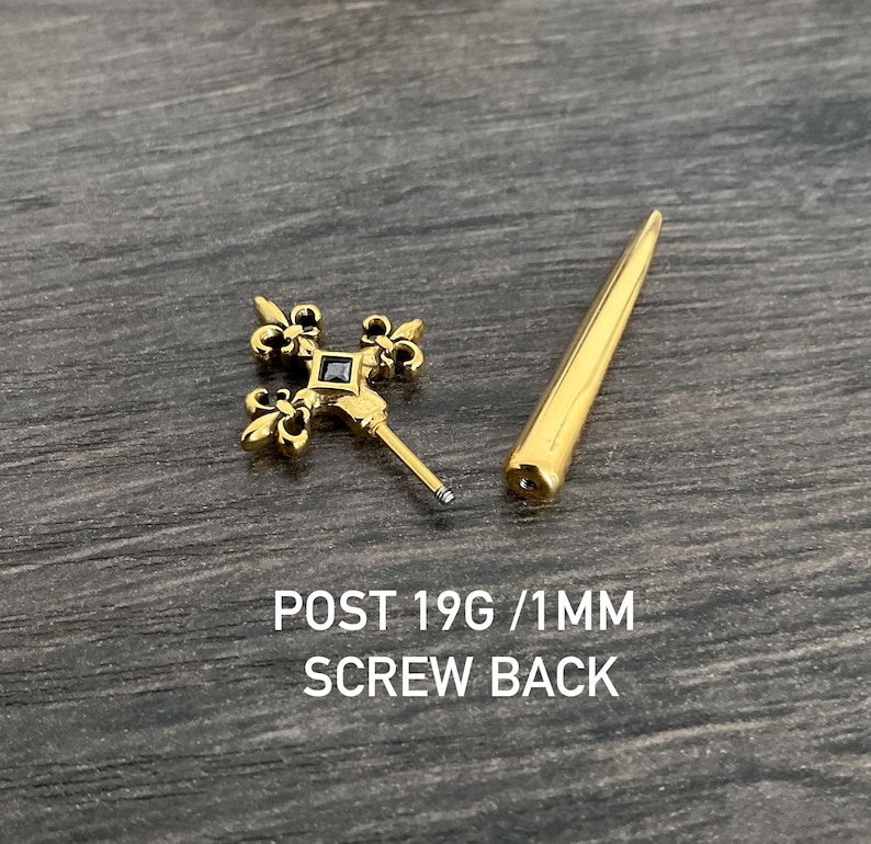 Pu&ograve; includere: Gioiello per il corpo color oro con una croce con dettagli a giglio e una gemma nera al centro. Il gioiello &egrave; fornito con un perno a vite. POST 19G / 1MM SCREW BACK.
