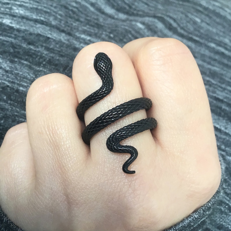 Puede incluir: Un anillo de serpiente negro con un dise&ntilde;o en espiral. El anillo se lleva en un dedo.