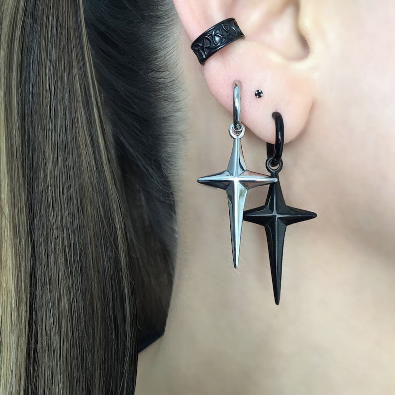 May include: A pair of earrings with a black and silver star design. The earrings are hanging from a hoop and a stud.
