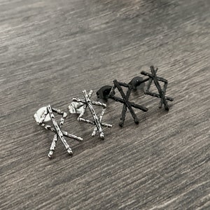 以下が含まれることがあります： 幾何学模様の銀と黒のイヤリング4つ。イヤリングは、テクスチャ加工された表面を持つ十字架の形をしています。