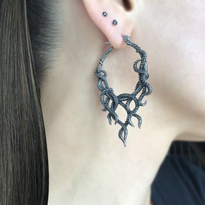 May include: Silver hoop earrings with a detailed octopus design. The octopus tentacles are curled and twisted, creating a dramatic and intricate look.