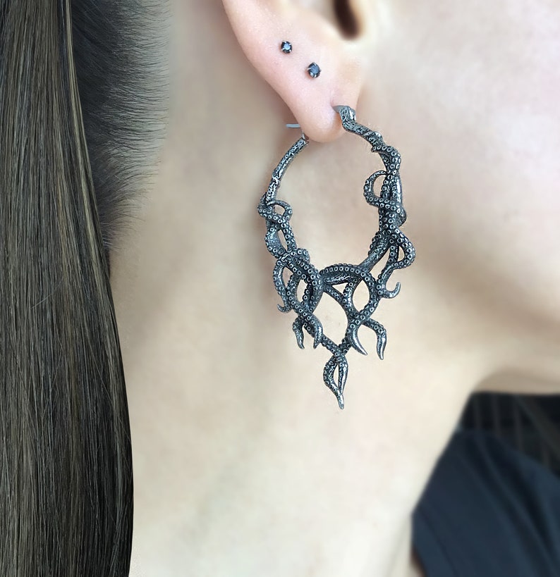 May include: Silver hoop earrings with a detailed octopus design. The octopus tentacles are curled and twisted, creating a dramatic and intricate look.