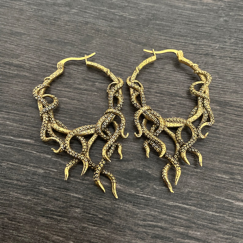 May include: A pair of gold-toned hoop earrings with an octopus design. The earrings are large and have a dangling design.