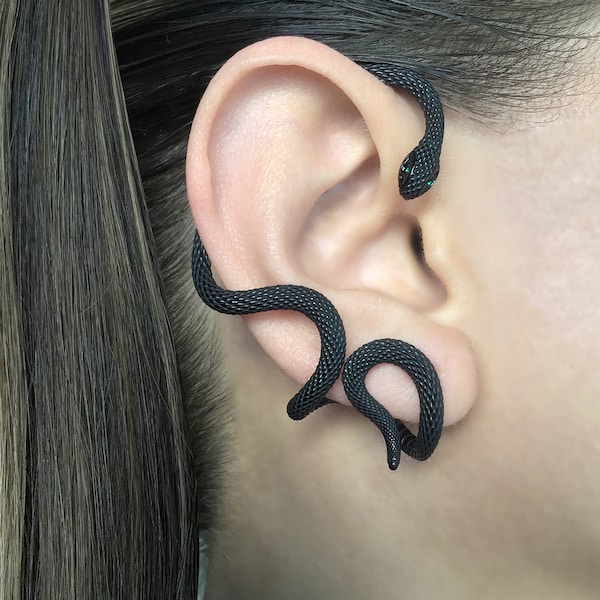 Può includere: Orecchino a forma di serpente nero con occhi verdi. Il serpente è avvolto attorno all'orecchio e ha una superficie testurizzata.
