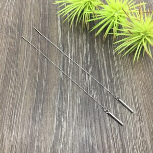 May include: A pair of silver chain earrings with a small bar pendant at the end of each chain.