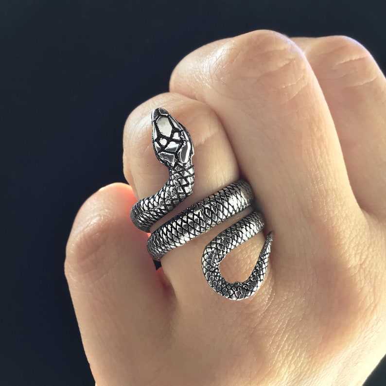 May include: A silver snake ring with a detailed textured design. The snake is coiled around the finger and the head is facing forward.
