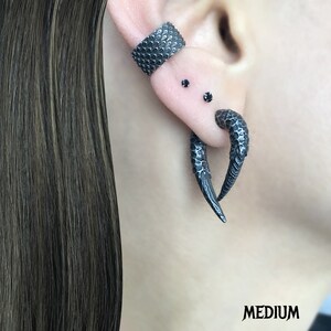 Peut inclure: Une boucle d'oreille noire textur&eacute;e avec deux clous d'oreille noirs. Un autre boucle d'oreille noire textur&eacute;e et incurv&eacute;e est &eacute;galement visible.
