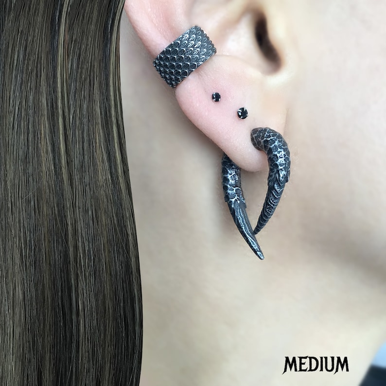 Peut inclure: Une boucle d'oreille noire textur&eacute;e avec deux clous d'oreille noirs. Un autre boucle d'oreille noire textur&eacute;e et incurv&eacute;e est &eacute;galement visible.