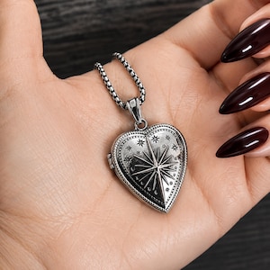 May include: A silver-toned heart-shaped locket pendant suspended from a textured box chain. The locket features an engraved North Star design surrounded by smaller star motifs and a beaded border, finished with an oxidised, darkened metal texture.