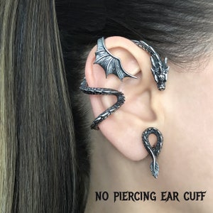 Puede incluir: Un pendiente de oreja de drag&oacute;n plateado con dise&ntilde;o de ala. El pendiente de oreja est&aacute; dise&ntilde;ado para usarse sin perforaci&oacute;n. "NO PIERCING EAR CUFF" est&aacute; escrito en texto negro en la parte inferior de la imagen.