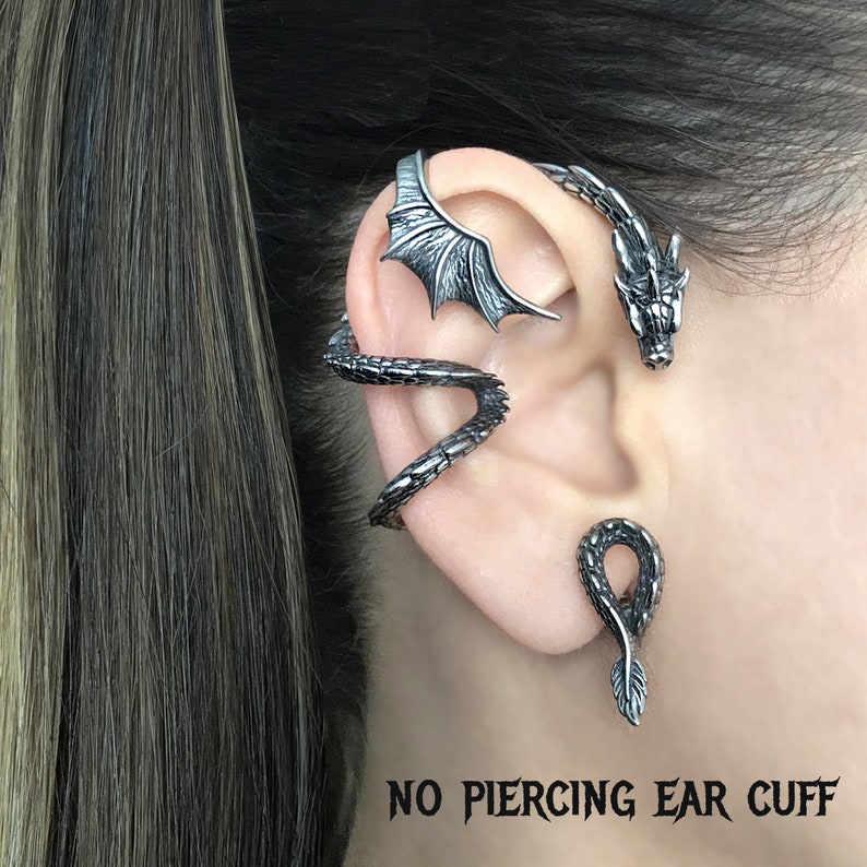 Puede incluir: Un pendiente de oreja de drag&oacute;n plateado con dise&ntilde;o de ala. El pendiente de oreja est&aacute; dise&ntilde;ado para usarse sin perforaci&oacute;n. "NO PIERCING EAR CUFF" est&aacute; escrito en texto negro en la parte inferior de la imagen.