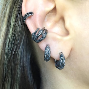 Puede incluir: Pendientes de aro negros con dise&ntilde;o de garra de drag&oacute;n. Los pendientes est&aacute;n hechos de metal y tienen un acabado negro.