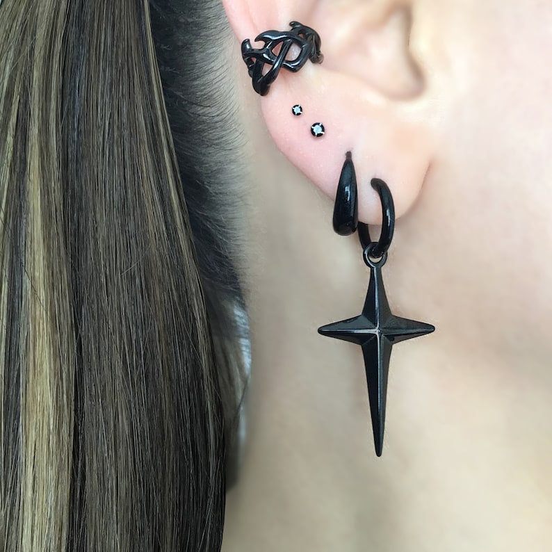 May include: Black ear cuff with a geometric design, two small black stud earrings, and a black hoop earring with a dangling star pendant.