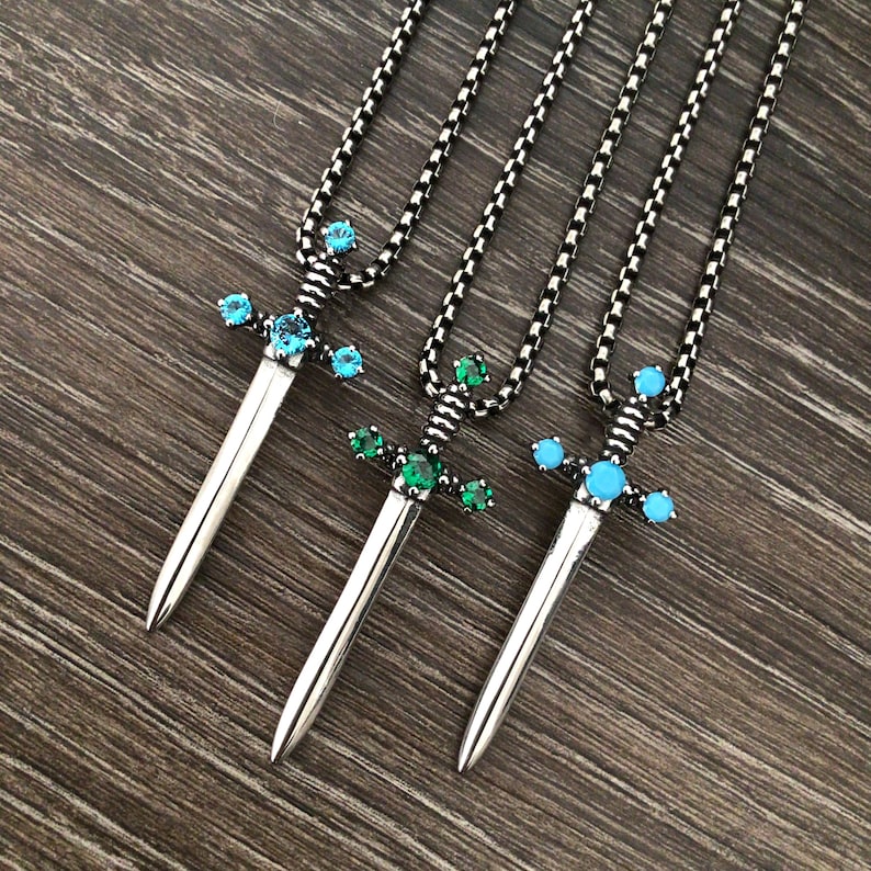 May include: Three silver sword necklaces with different coloured gemstones. The swords have blue, green, and turquoise gemstones.