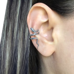 Puede incluir: Un brazalete de oreja de serpiente de plata. La serpiente est&aacute; enroscada alrededor de la oreja y tiene un dise&ntilde;o texturizado y escamoso.