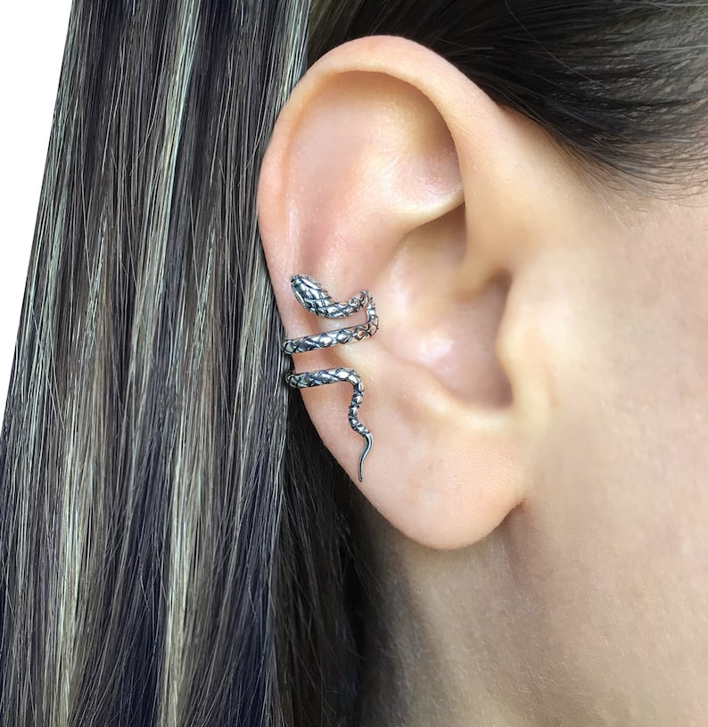 Puede incluir: Un brazalete de oreja de serpiente de plata. La serpiente est&aacute; enroscada alrededor de la oreja y tiene un dise&ntilde;o texturizado y escamoso.