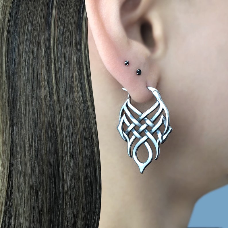 May include: Silver hoop earrings with a detailed, intricate, woven design. The earrings are in the shape of a teardrop.