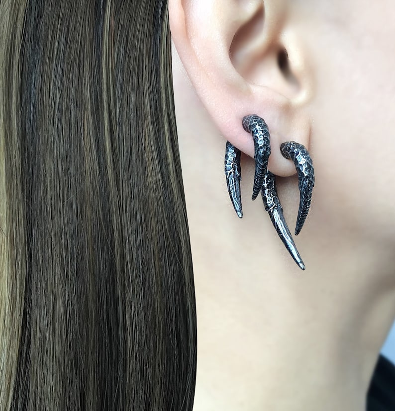 Peut inclure: Une paire de boucles d'oreilles en forme de griffe noire. Les boucles d'oreilles sont en m&eacute;tal et ont une surface textur&eacute;e.