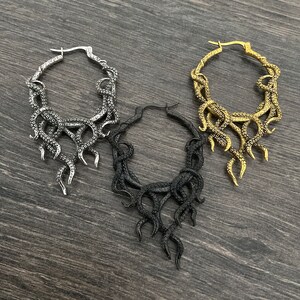 May include: Three hoop earrings with a dangling octopus design. The earrings are silver, gold, and black.