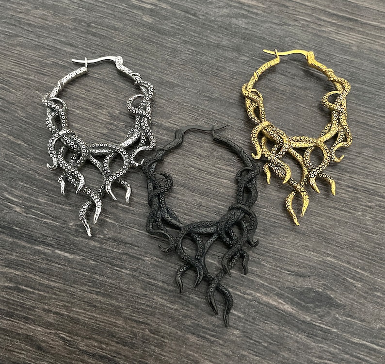May include: Three hoop earrings with a dangling octopus design. The earrings are silver, gold, and black.