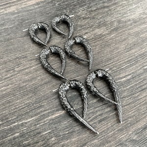 Peut inclure: Cinq paires de boucles d'oreilles en m&eacute;tal noir avec une texture martel&eacute;e et une forme pointue et incurv&eacute;e. Les boucles d'oreilles sont dispos&eacute;es en quinconce sur une surface en bois.