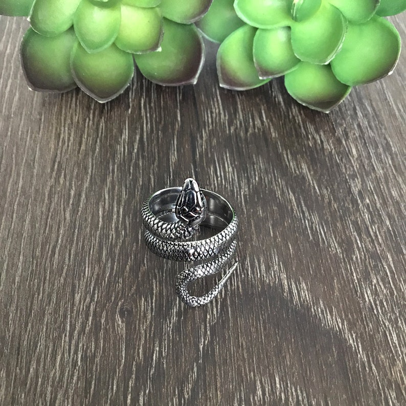 May include: A silver snake ring with a coiled body and a detailed head. The ring is on a wooden surface.