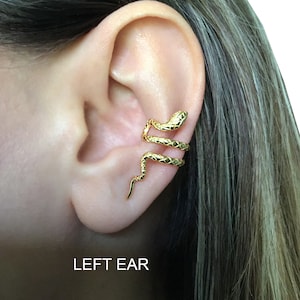 Puede incluir: Un pendiente de oreja de serpiente de oro. La serpiente est&aacute; enroscada alrededor de la oreja y tiene una superficie texturizada. El pendiente de oreja se lleva en la oreja izquierda. El texto "LEFT EAR" es visible debajo de la oreja.