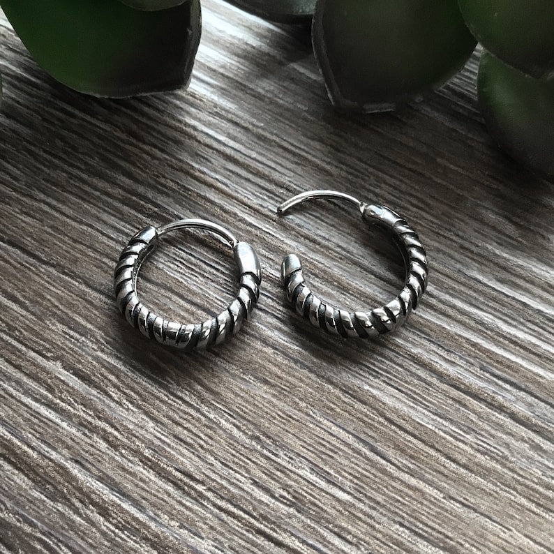 May include: Two silver hoop earrings with a twisted rope design. The earrings are on a wooden surface.