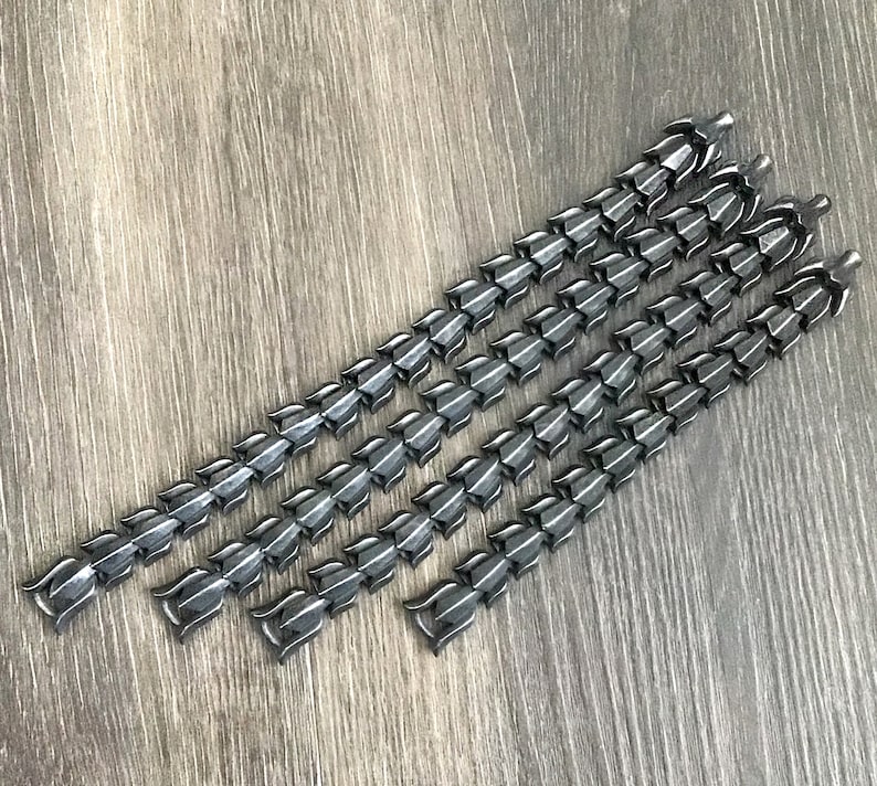 Puede incluir: Cinco cadenas de metal negro con un dise&ntilde;o de eslab&oacute;n &uacute;nico. Cada cadena tiene una serie de eslabones conectados, puntiagudos y en forma de l&aacute;grima.