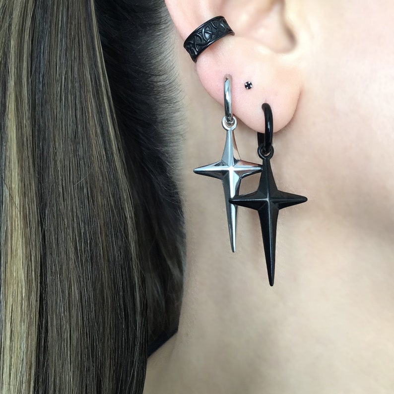 May include: A pair of earrings with a black star and a silver star pendant. The earrings are hanging from a black hoop and a silver hoop.