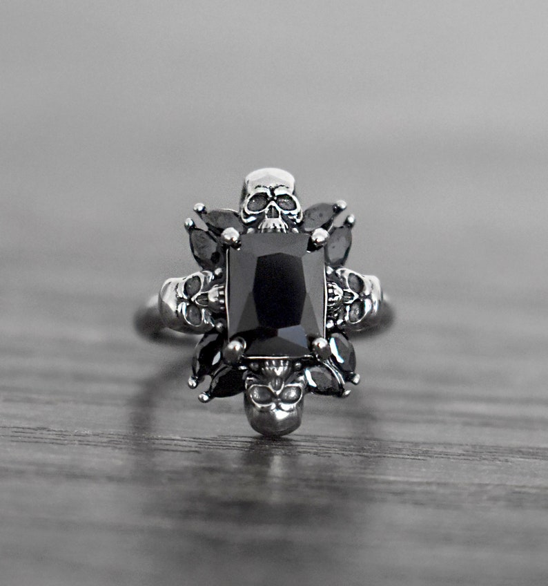 May include: A silver ring featuring a black gemstone surrounded by skull details.