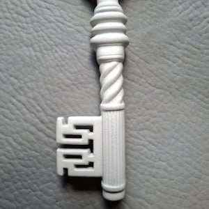 May include: A white decorative key with a detailed design. The key features a twisted stem and ornate head. The key's bit has a unique, geometric shape. The key is set against a gray background.