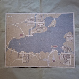 Pode incluir: Um mapa detalhado de Silent Hill, apresentando o layout da cidade com estradas, edifícios e o Lago Toluca. O mapa tem uma estética vintage com um esquema de cores bege e azul, e inclui texto como "Old Silent Hill" e "Central Silent Hill".